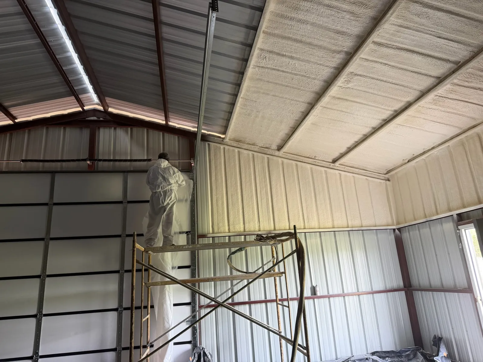 Crew member spraying foam inside a commercial metal building